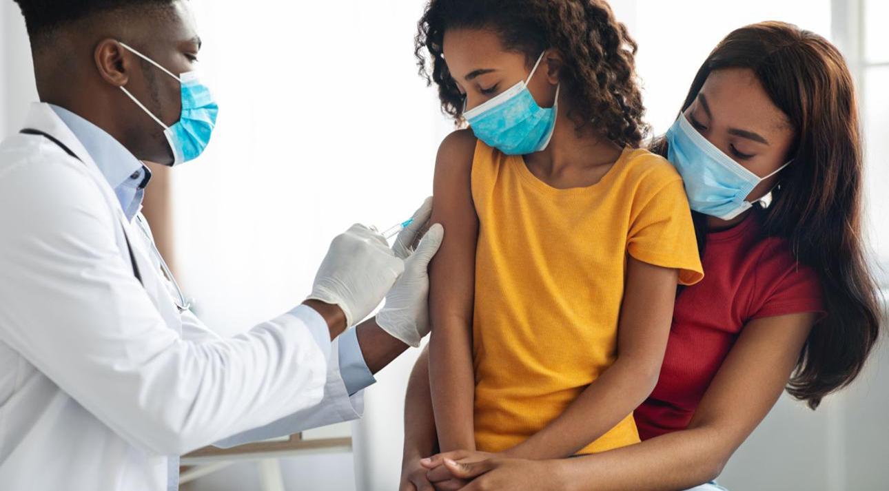 A Black doctor vaccinating a young patient held by her mother